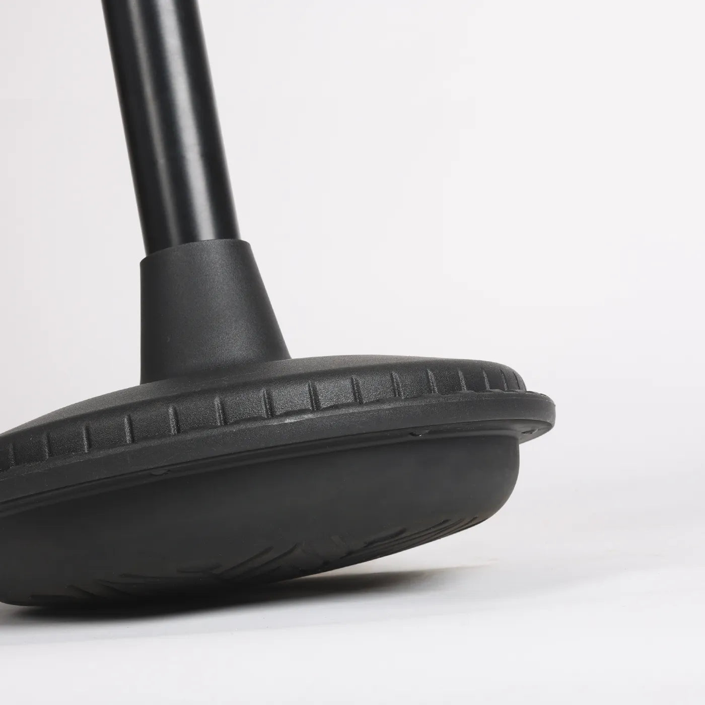 Close-up photography of bottom part of foot from black Wobblez Settle, Stable or Spine wobble stool, a faux leather black office chair with a white background