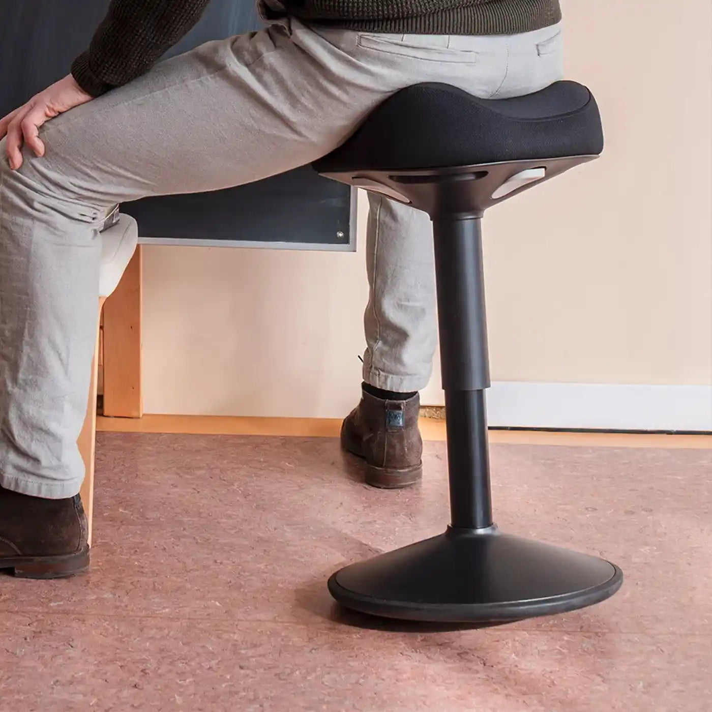 Person with kaki/taupe pants and brown leather shoes sitting in classroom on a all black Wobblez Soothe wobble stool