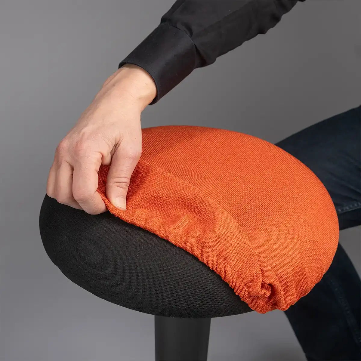 Detailed photography of person pulling a Coral Orange Wobblez Skins cover on a black Spine wobble stool against a gray background