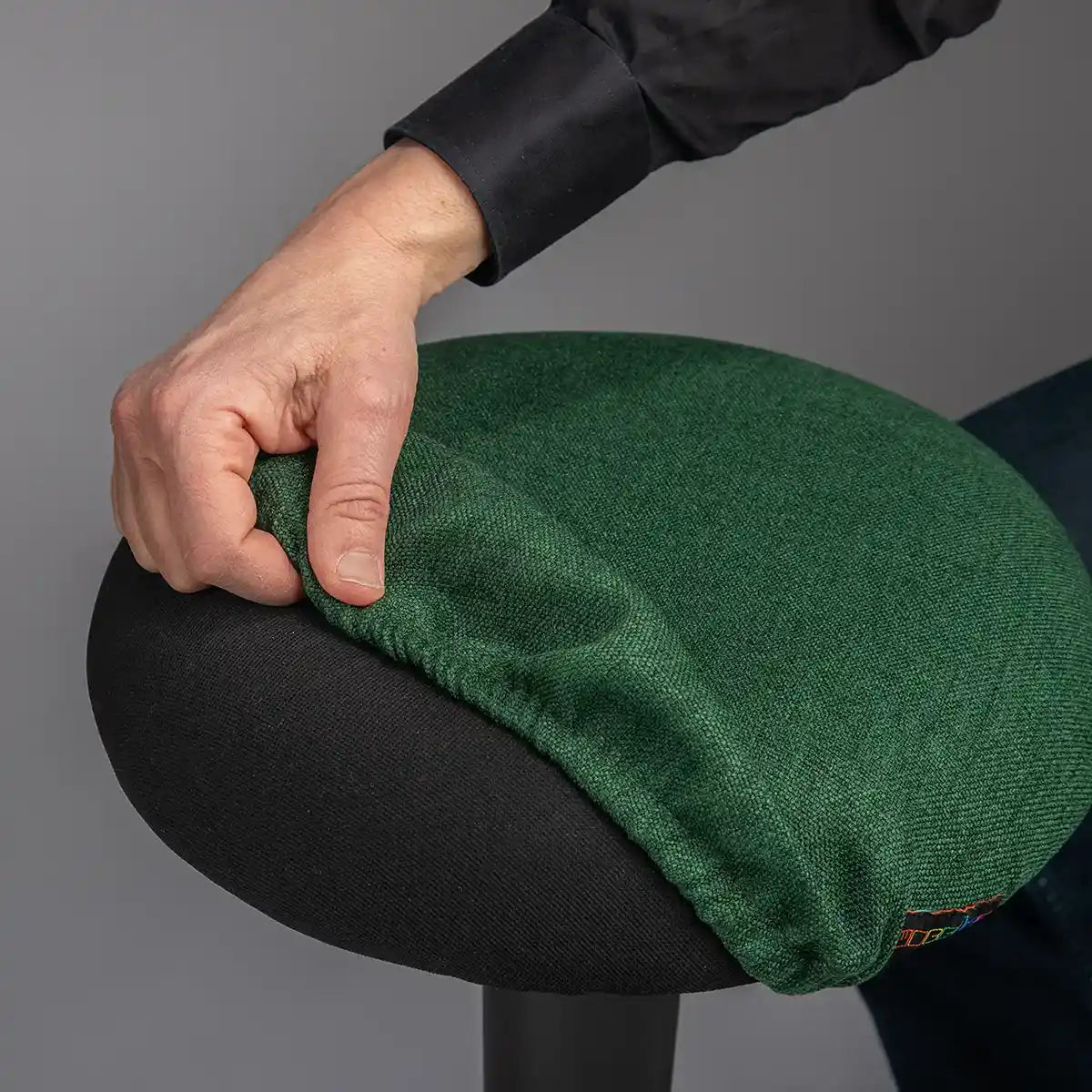 Detailed photography of person pulling a Forest Green Wobblez Skins cover on a black Spine wobble stool against a gray background