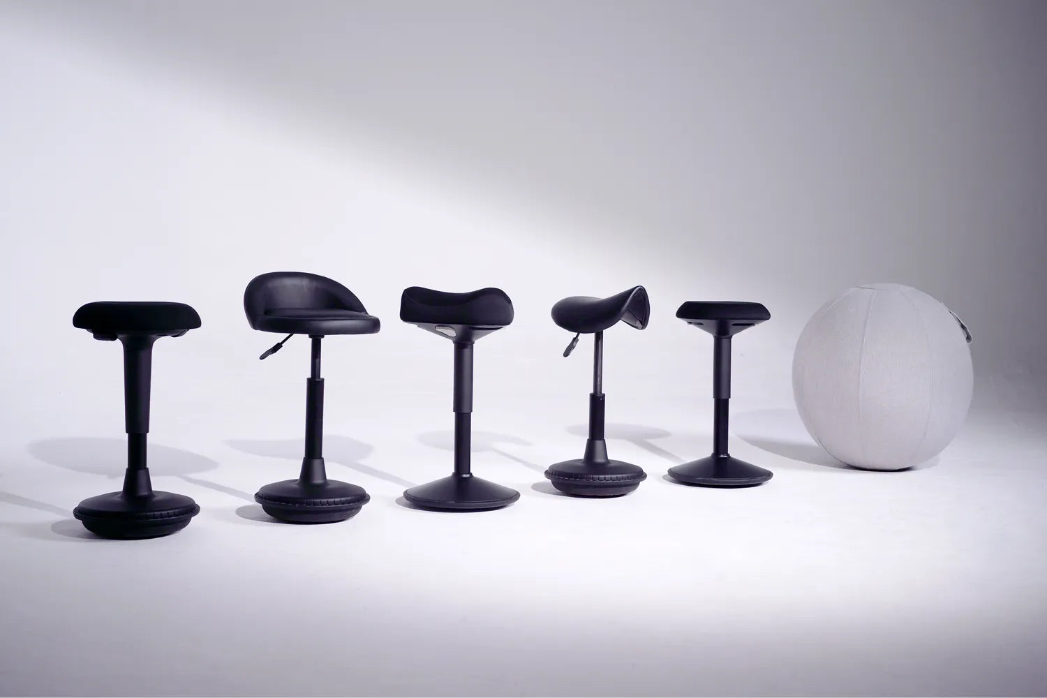 The whole collection of black Wobblez wobble stools and a gray sitting ball in a film studio next to each other