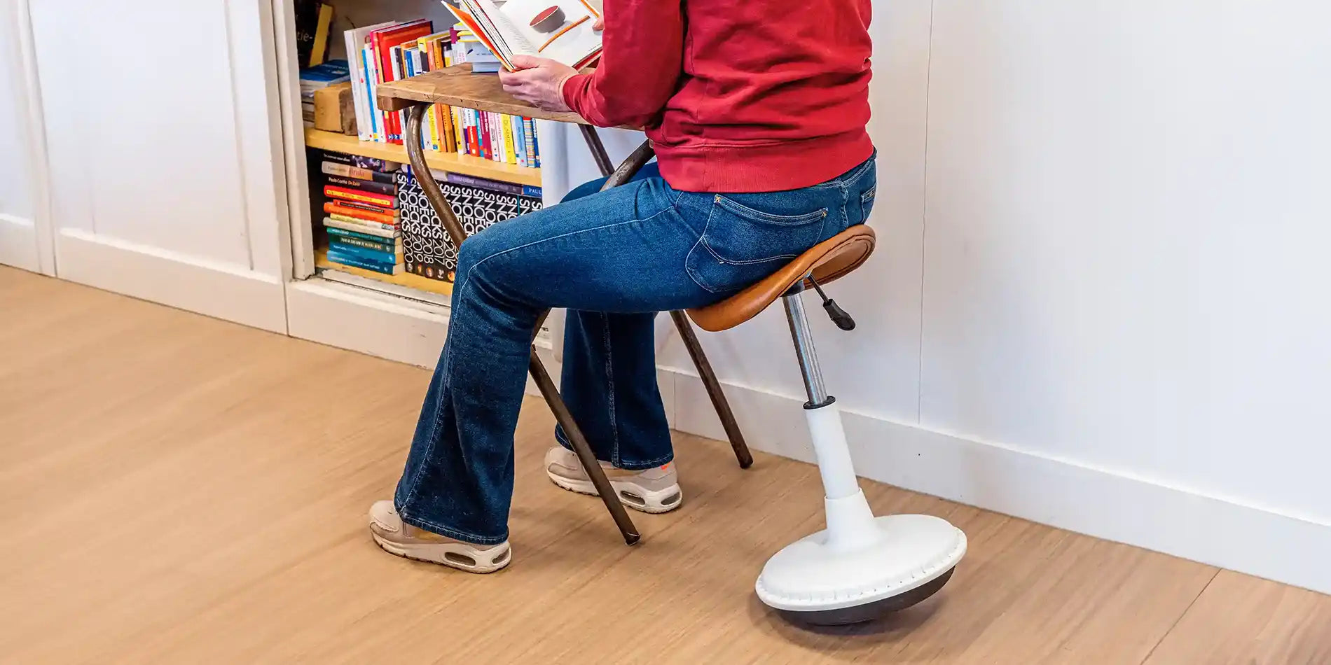 Person reading a book at a wooden desk using a white and cognac faux leather adjustable Wobblez Stable wobble stool in a room with books.