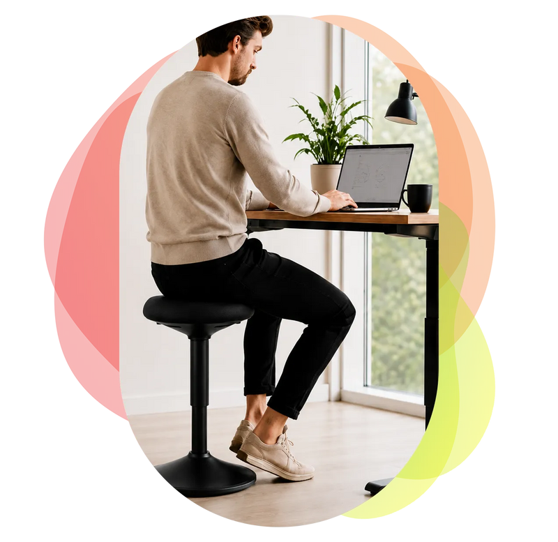 Man sitting on a black Wobblez height-adjustable wobble stool working on a laptop at a desk with a plant and mug.