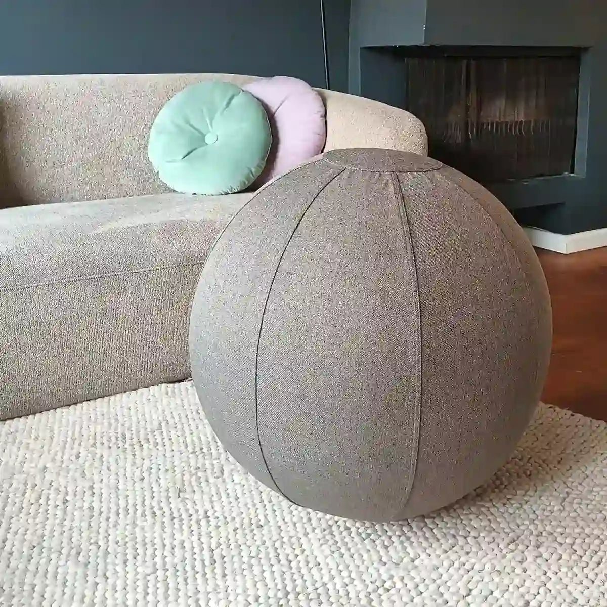 Gray fabric Wobblez sitting exercise ball in a living room setting with a sofa and cushions.