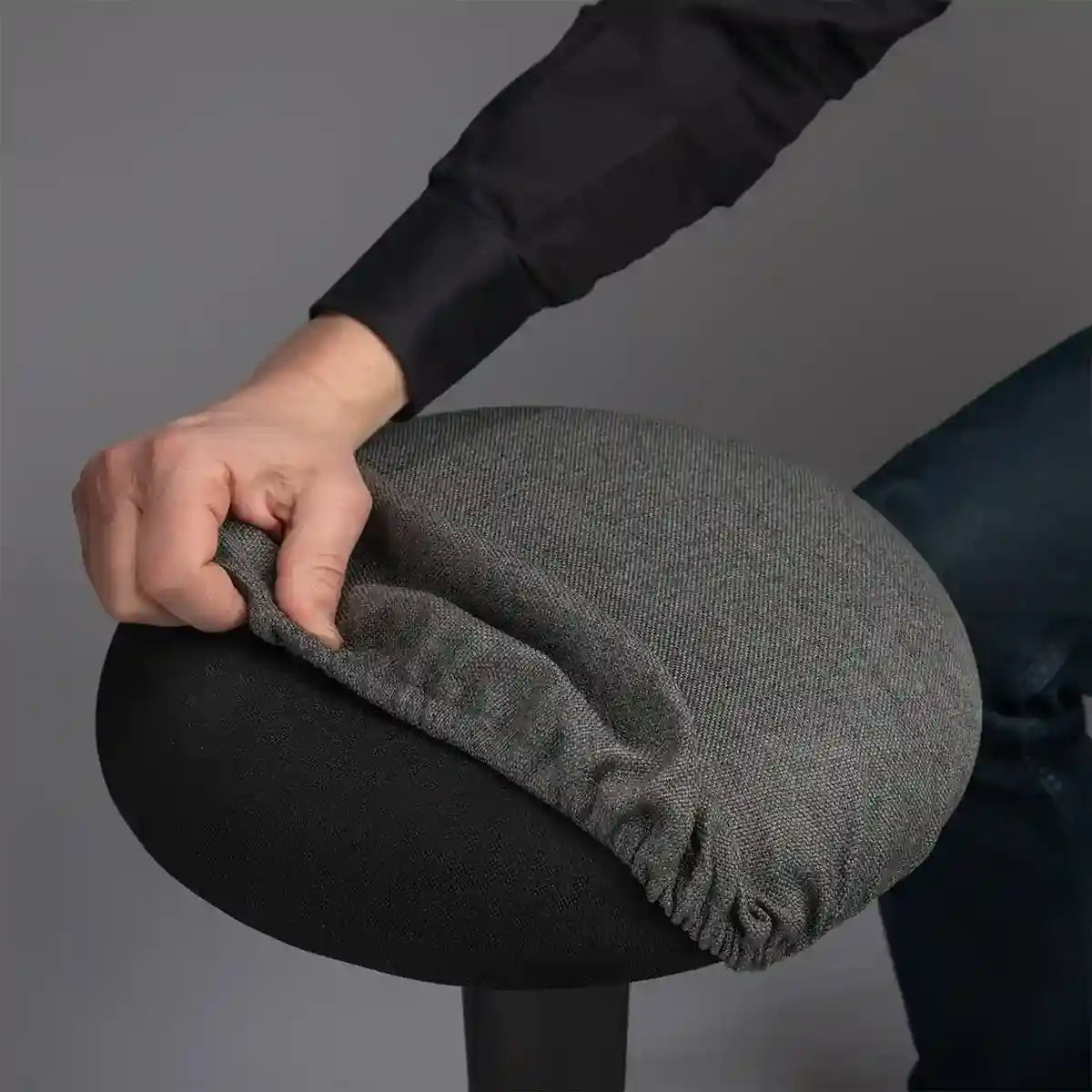 Detailed photography of person pulling a Anthracite Wobblez Skins cover on a black Spine wobble stool against a gray background