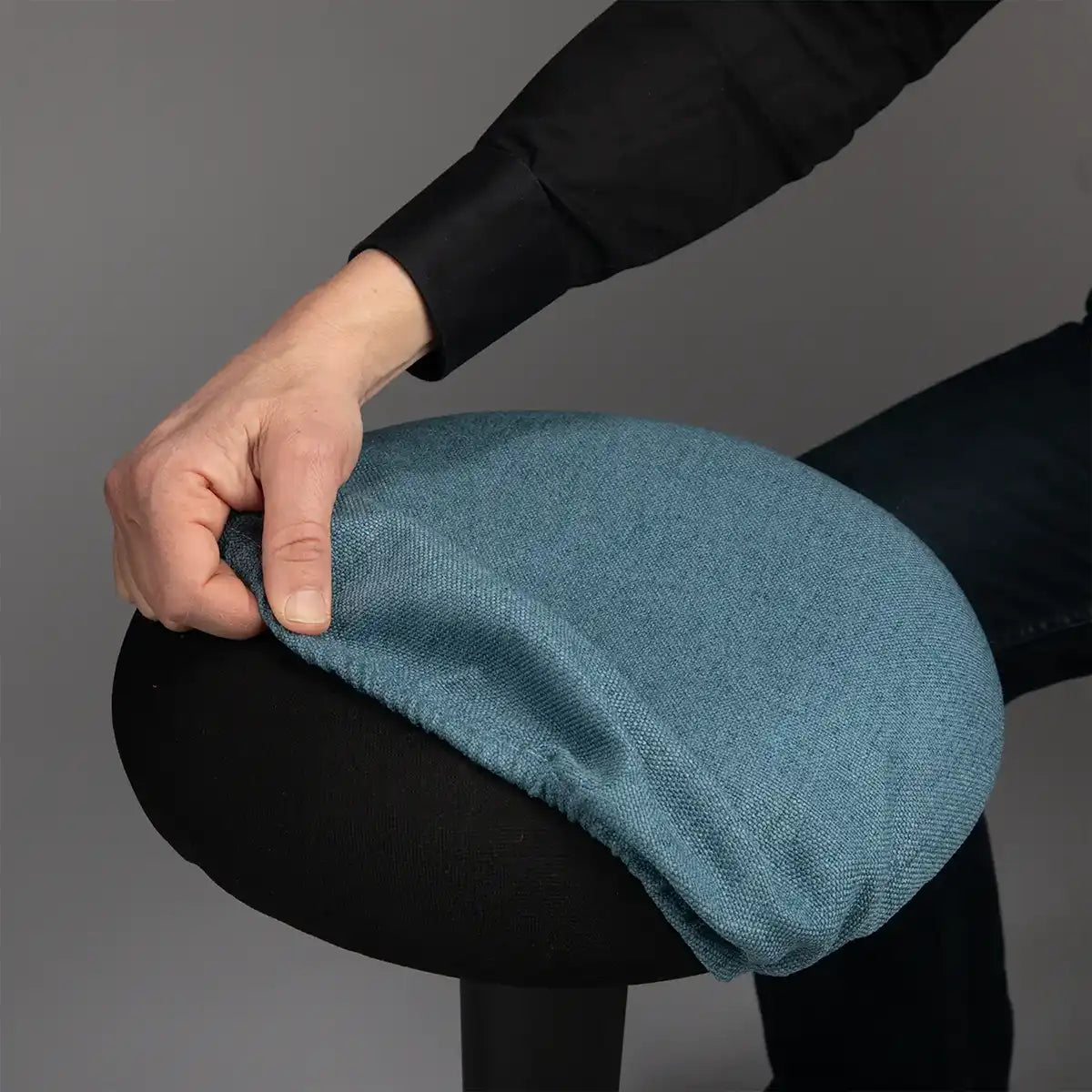 Detailed photography of person pulling a Blue Wobblez Skins cover on a black Spine wobble stool against a gray background