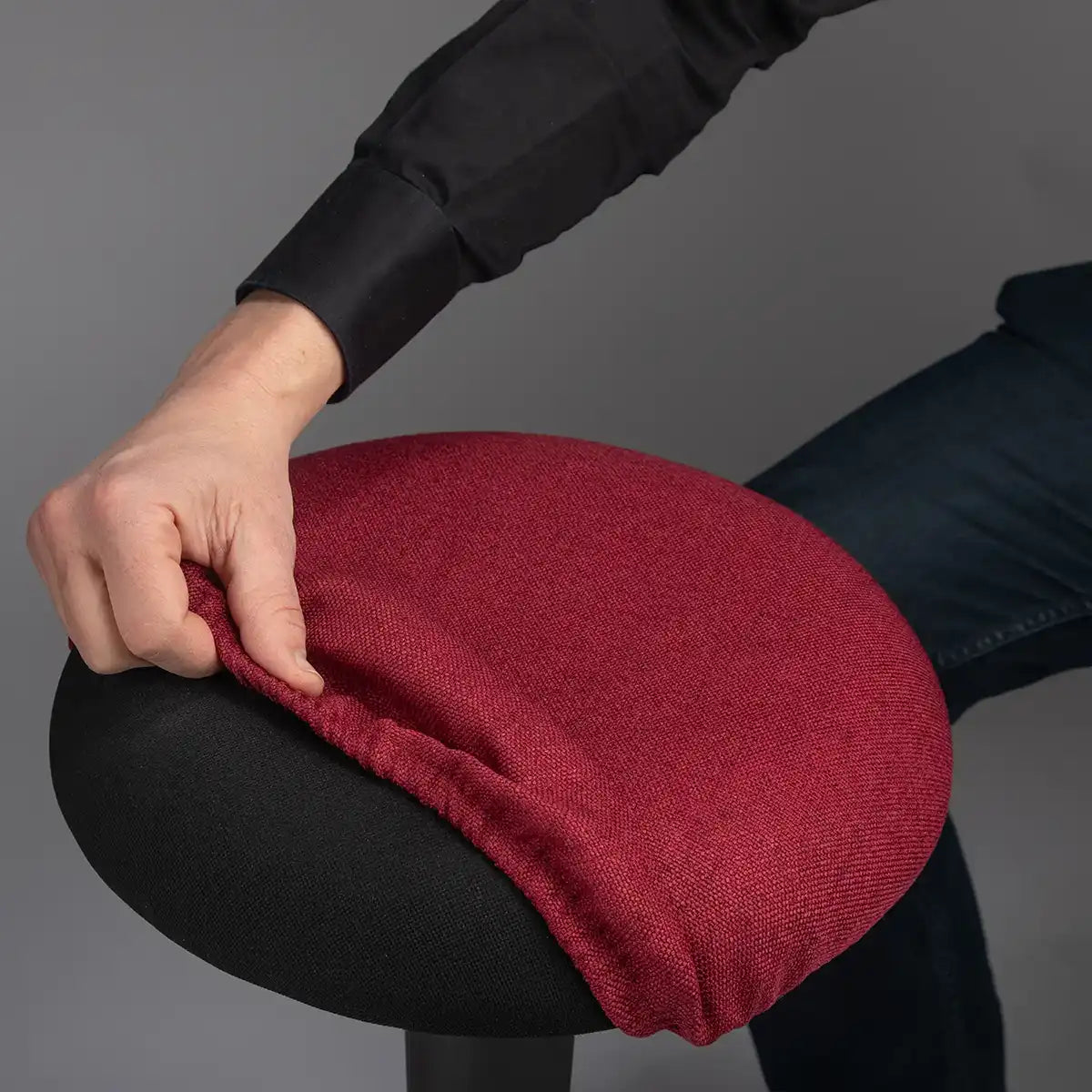 Detailed photography of person pulling a Bordeaux Red Wobblez Skins cover on a black Spine wobble stool against a gray background
