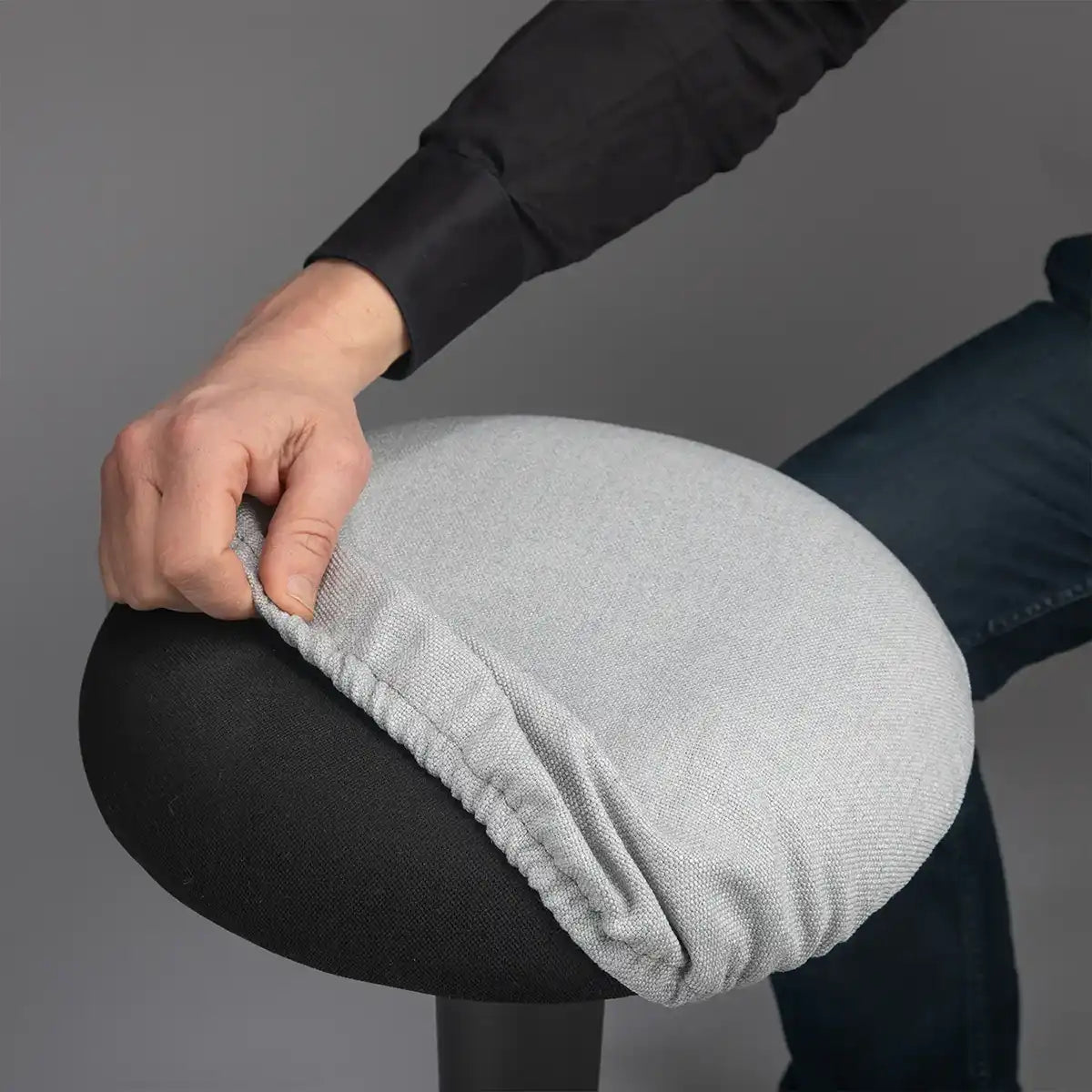 Detailed photography of person pulling a Metallic Grey Wobblez Skins cover on a black Spine wobble stool against a gray background