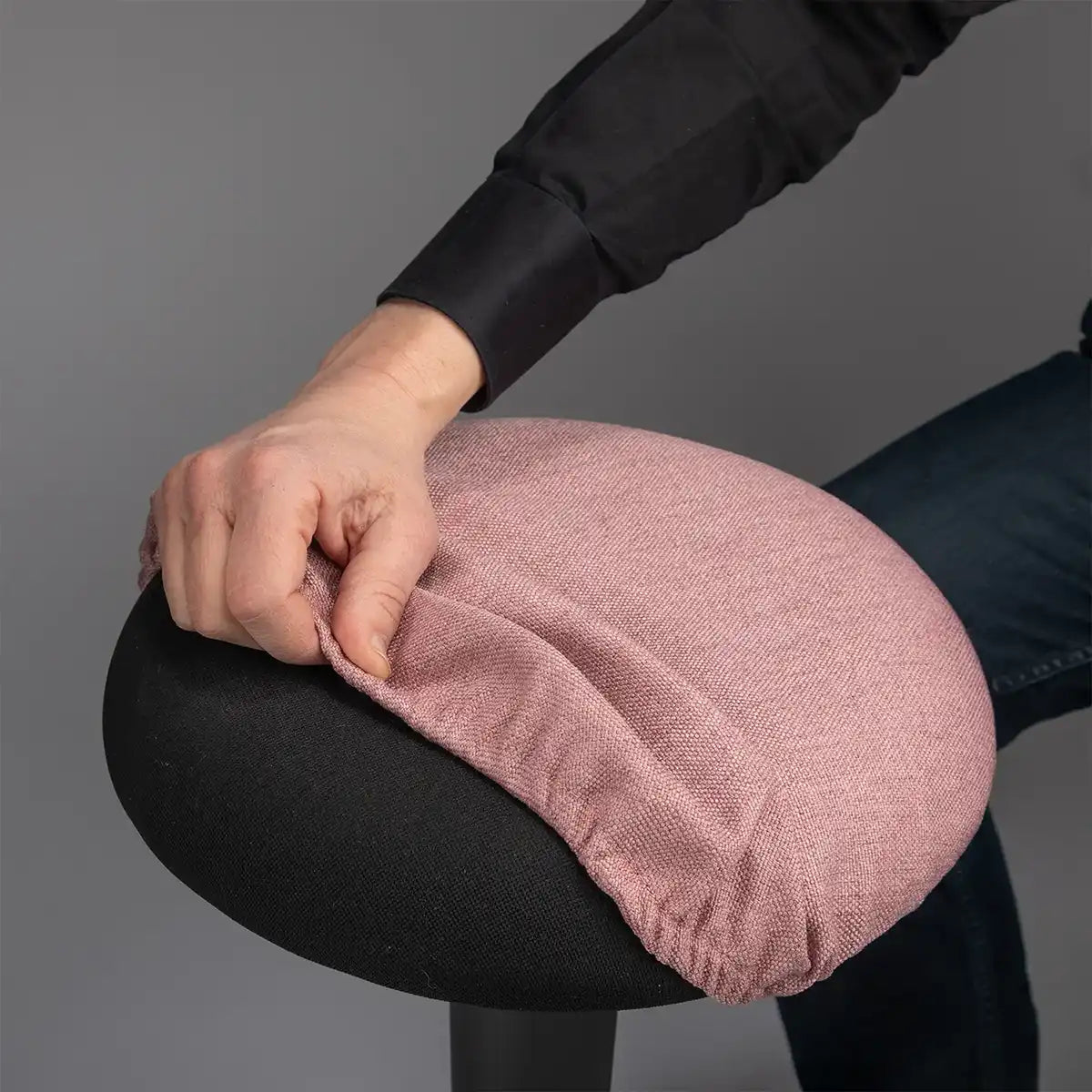 Detailed photography of person pulling a Dusty Pink Wobblez Skins cover on a black Spine wobble stool against a gray background