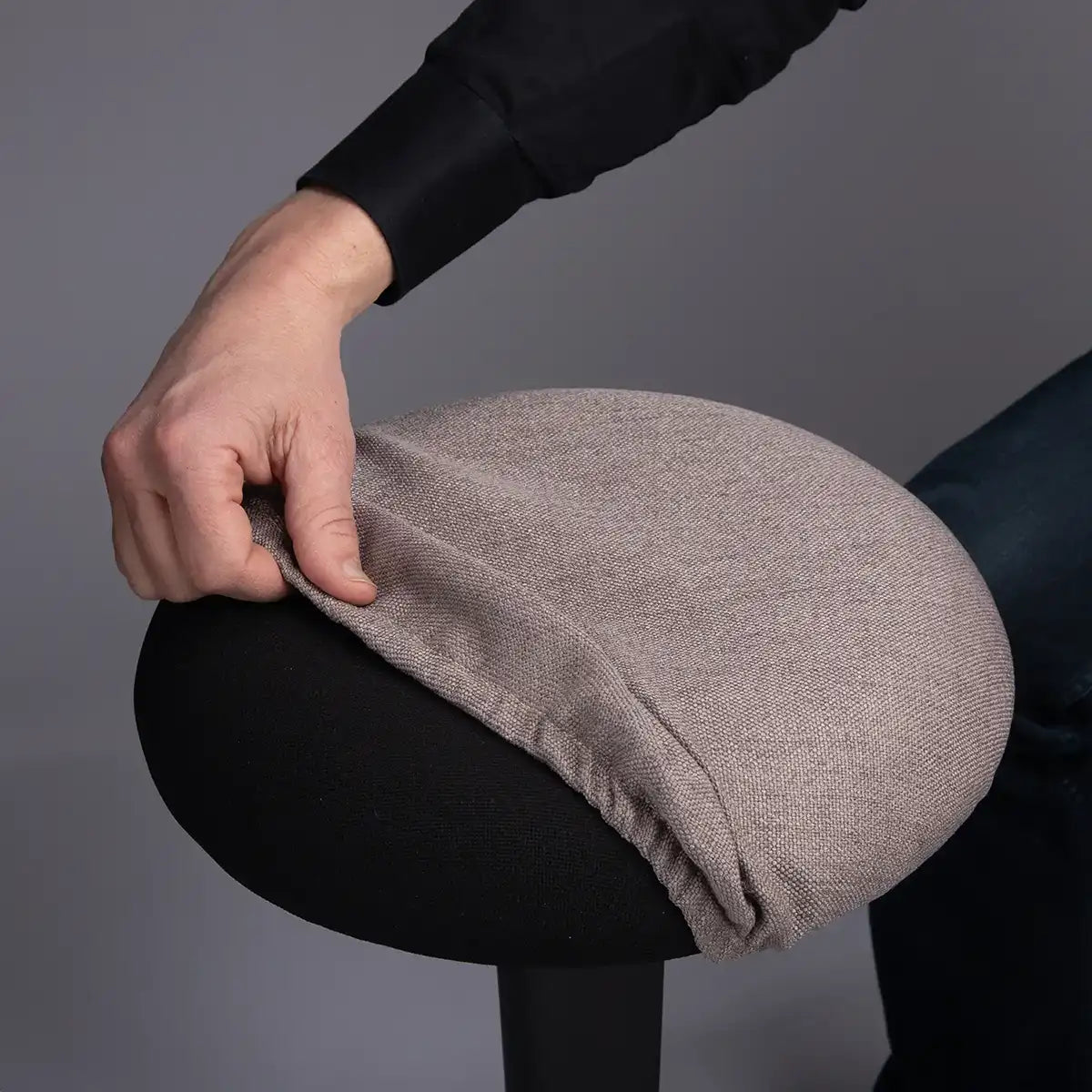 Detailed photography of person pulling a Taupe Wobblez Skins cover on a black Spine wobble stool against a gray background