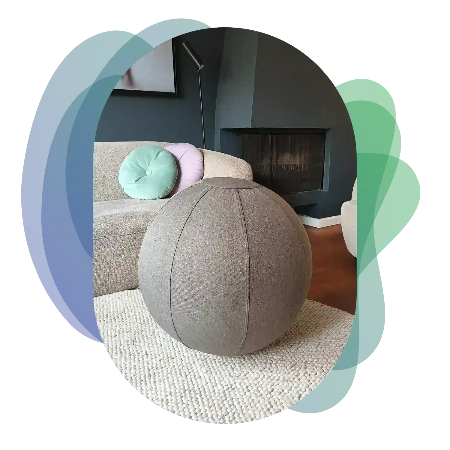 A gray 65cm fabric Wobblez exercise sitting ball sits on a textured white rug in a living room with a couch and cushions in the background.