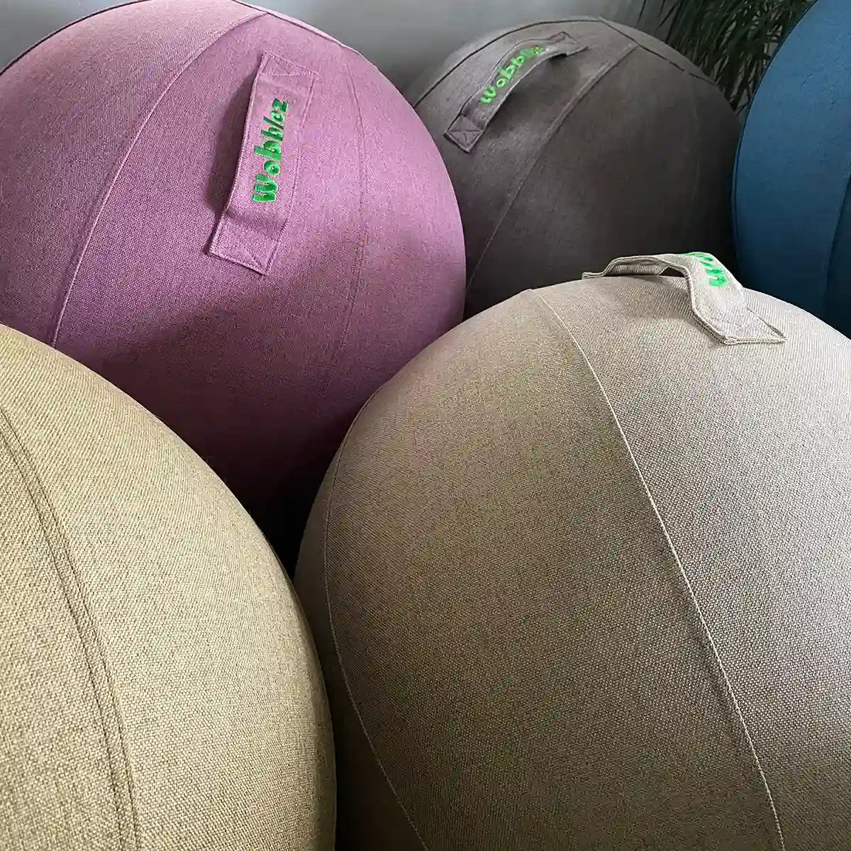 Several Wobblez Sphere fabric sitting exercise balls in muted colors, each with a handle are grouped closely together.